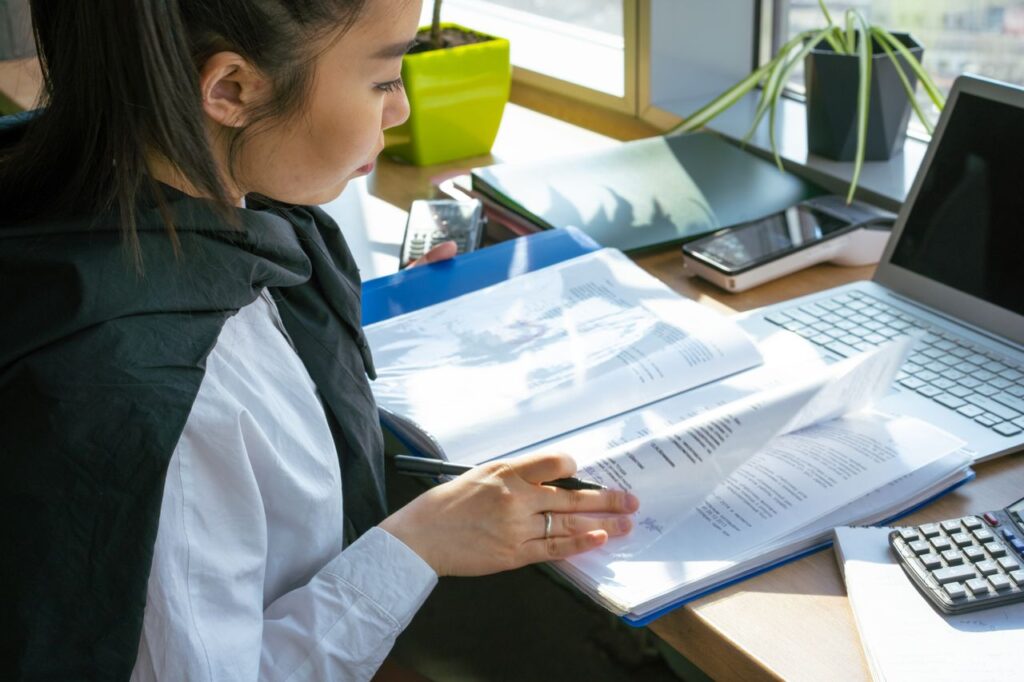 Vrouw bladert in map op bureau met rekenmachine en laptop ernaast | MBO Kompas